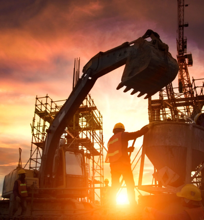 Silhouette of construction workers and excavator bucket against a sunset sky at an industrial site.